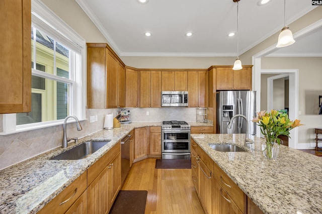 kitchen with light wood-style flooring, stainless steel appliances, crown molding, and a sink