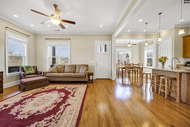 living room with light wood-type flooring, a ceiling fan, recessed lighting, crown molding, and baseboards