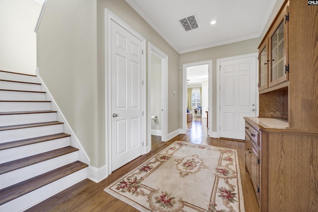 interior space with wood finished floors, baseboards, visible vents, ornamental molding, and stairs