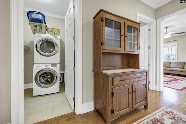 clothes washing area featuring stacked washer / drying machine, baseboards, light wood-style floors, and crown molding