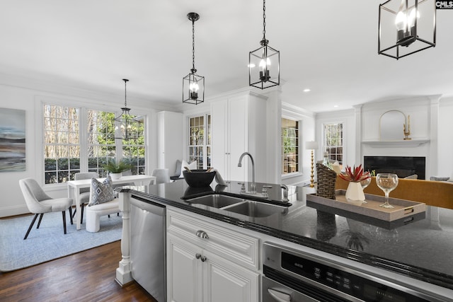 kitchen with crown molding, stainless steel dishwasher, dark wood-style floors, a glass covered fireplace, and a sink