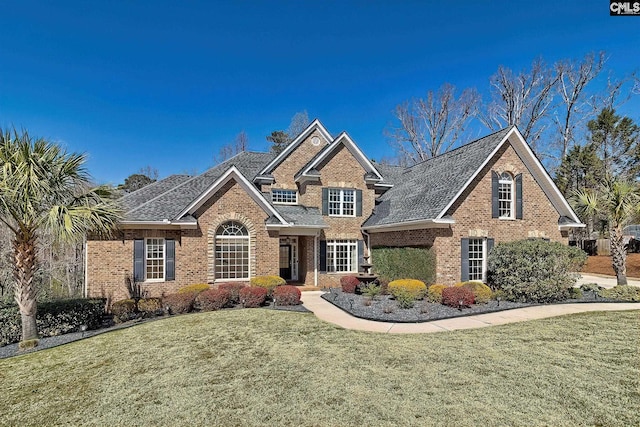 traditional-style home with brick siding, a front lawn, and roof with shingles