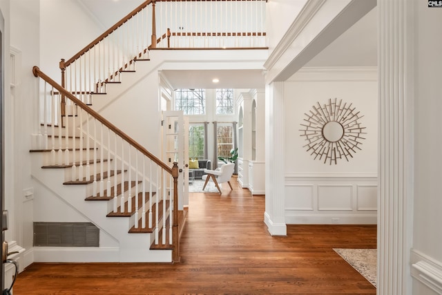 entryway featuring visible vents, crown molding, a high ceiling, wood finished floors, and a decorative wall