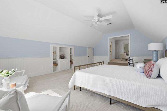 bedroom with visible vents, a wainscoted wall, vaulted ceiling, light carpet, and a ceiling fan