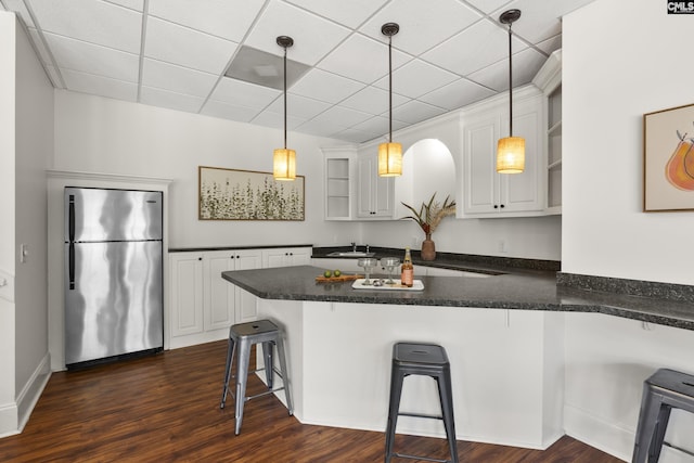 kitchen featuring open shelves, a peninsula, stainless steel refrigerator, white cabinetry, and dark countertops