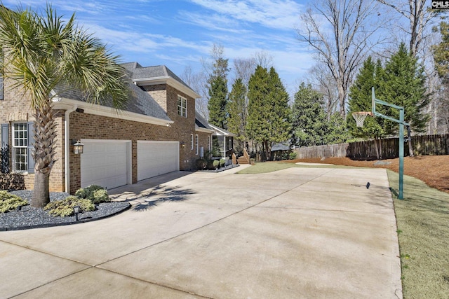 view of side of home with driveway, fence, roof with shingles, an attached garage, and brick siding