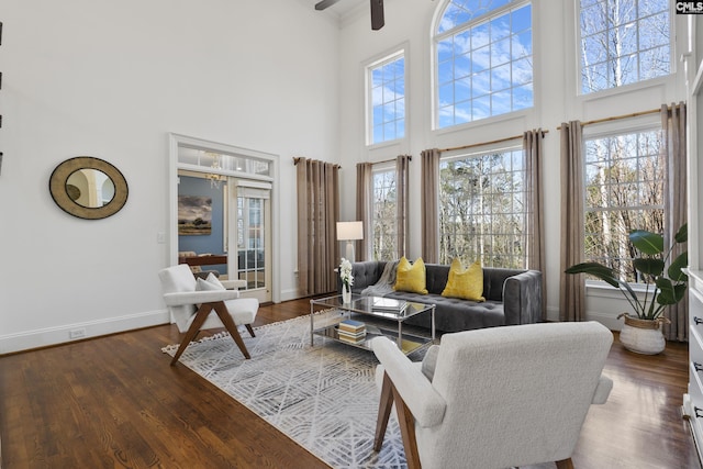 living area with a towering ceiling, ceiling fan, baseboards, and wood finished floors