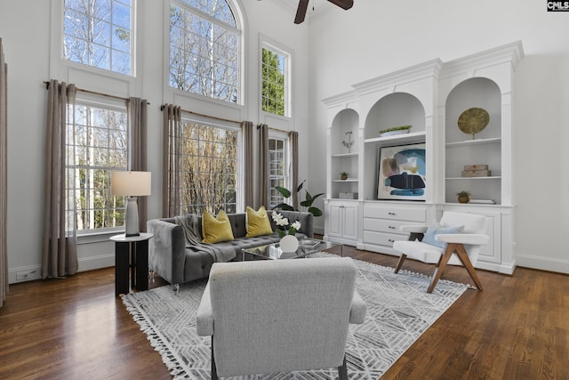 living area with a towering ceiling, baseboards, ceiling fan, and dark wood-style flooring