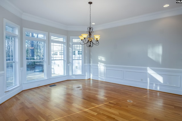 unfurnished dining area with a notable chandelier, crown molding, a wainscoted wall, and wood finished floors