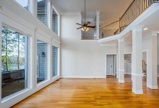 unfurnished living room with light wood-type flooring, decorative columns, baseboards, and ceiling fan