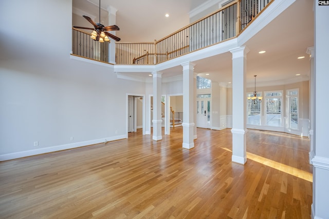 unfurnished living room featuring baseboards, ornate columns, ornamental molding, ceiling fan with notable chandelier, and light wood-type flooring