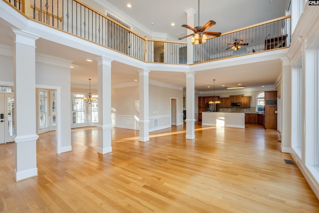 unfurnished living room with ceiling fan with notable chandelier, light wood-style flooring, ornamental molding, and ornate columns