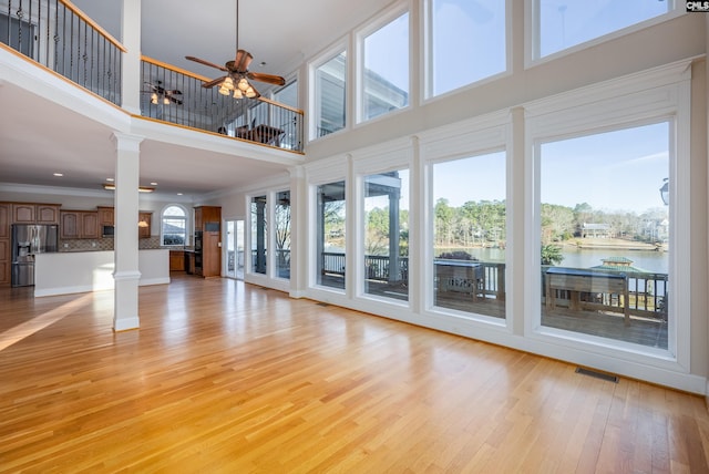 unfurnished living room with a healthy amount of sunlight, light wood-style floors, ornate columns, and a water view