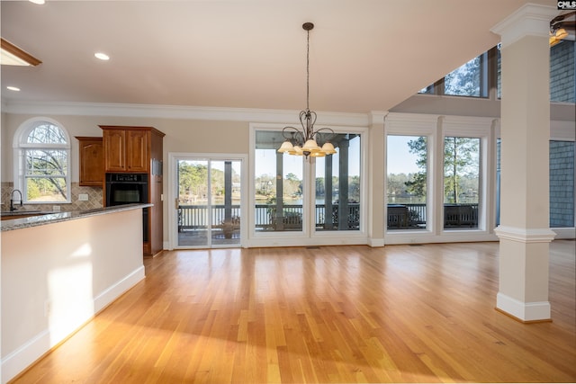 unfurnished dining area featuring light wood-type flooring, an inviting chandelier, crown molding, and ornate columns