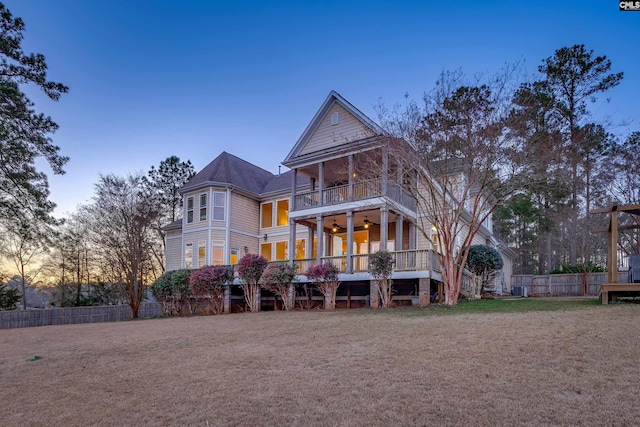 rear view of house with a lawn, a ceiling fan, fence, stairway, and a balcony