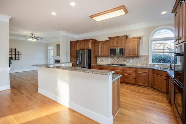 kitchen featuring brown cabinetry, light wood-style flooring, stainless steel appliances, crown molding, and a center island