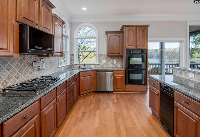 kitchen with light wood finished floors, ornamental molding, dark stone countertops, black appliances, and a sink