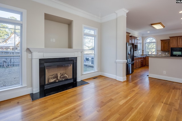 unfurnished living room with ornamental molding, a glass covered fireplace, light wood-style floors, decorative columns, and baseboards