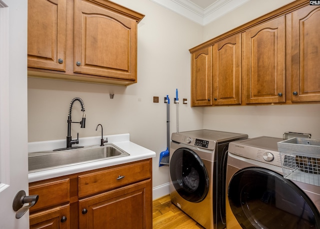 laundry area featuring cabinet space, ornamental molding, a sink, light wood-style floors, and washing machine and dryer