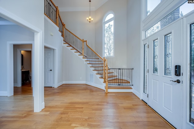 entrance foyer with baseboards, stairway, ornamental molding, a high ceiling, and light wood-style floors