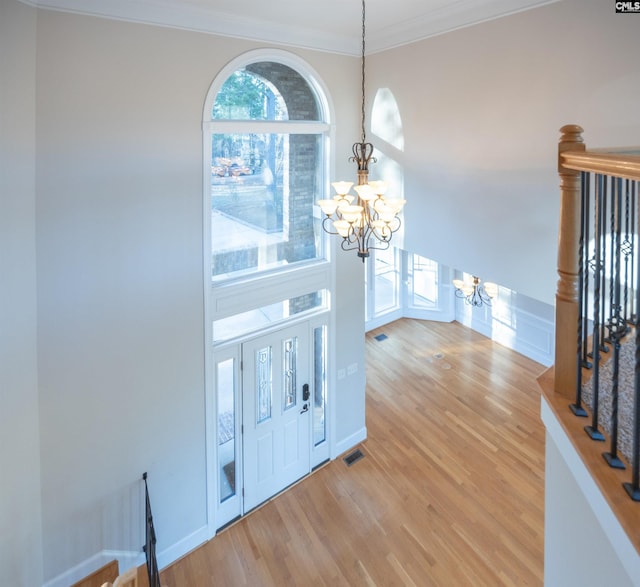 foyer entrance featuring visible vents, crown molding, stairway, light wood-style flooring, and a notable chandelier