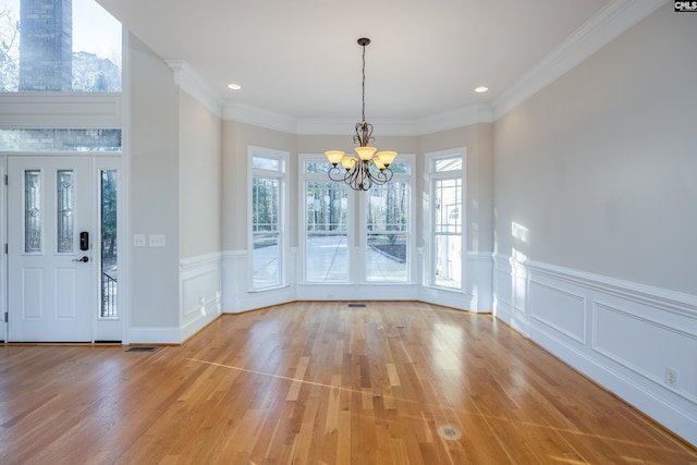 unfurnished dining area featuring light wood-style flooring, a notable chandelier, wainscoting, and ornamental molding