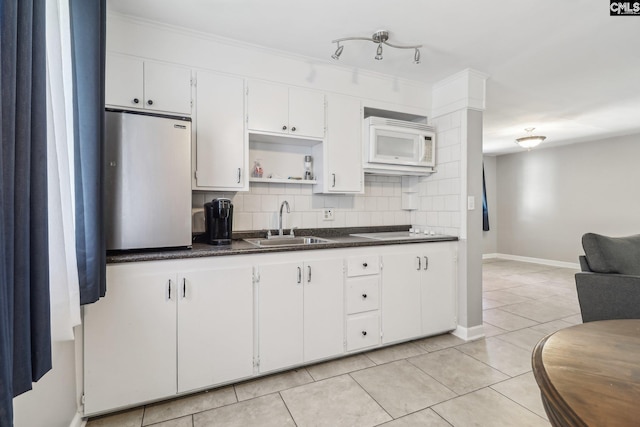 kitchen featuring light tile patterned floors, white microwave, a sink, dark countertops, and tasteful backsplash