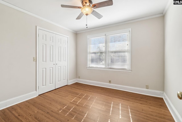 unfurnished bedroom with ornamental molding, wood finished floors, a closet, baseboards, and ceiling fan