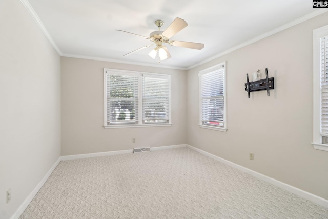 carpeted spare room with crown molding, a ceiling fan, baseboards, and visible vents