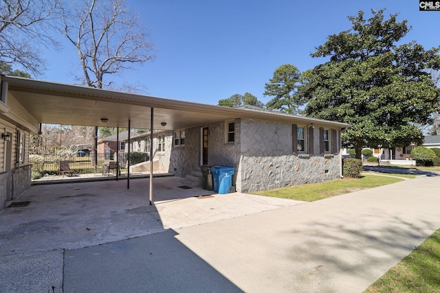 view of front of property with driveway, entry steps, stone siding, fence, and a carport