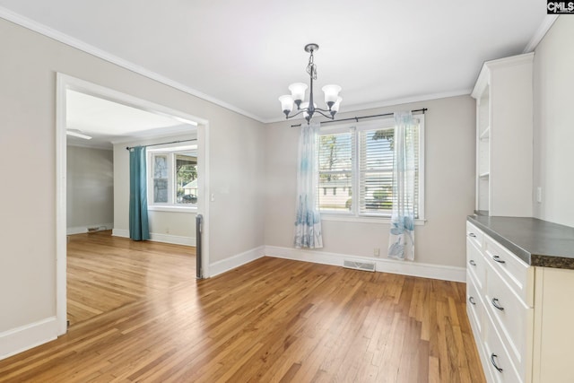 unfurnished dining area featuring baseboards, visible vents, light wood finished floors, crown molding, and a chandelier