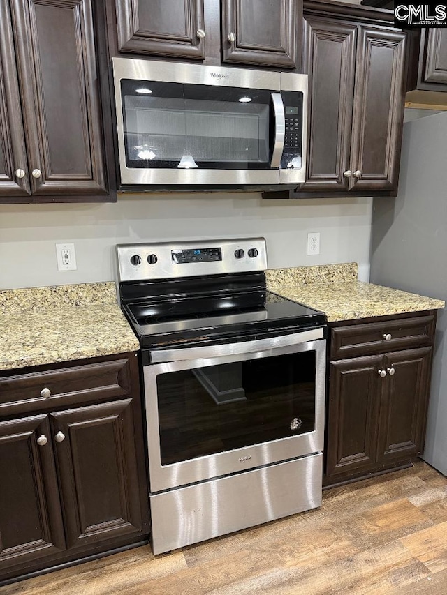 kitchen with stainless steel appliances, light stone countertops, dark brown cabinets, and light wood-style flooring