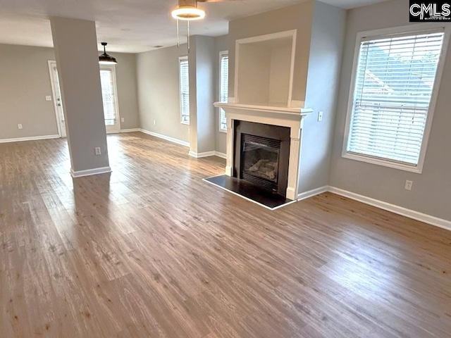 unfurnished living room featuring a glass covered fireplace, plenty of natural light, wood finished floors, and baseboards