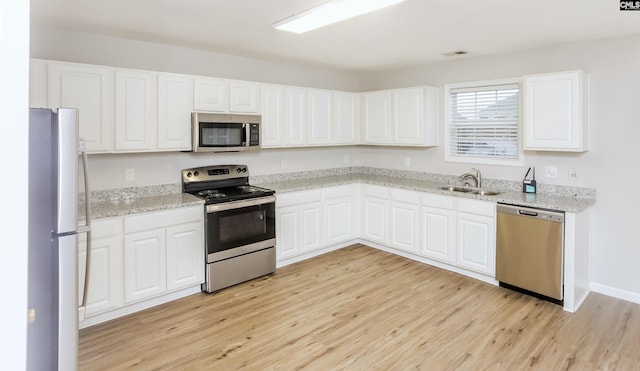 kitchen with light stone counters, a sink, stainless steel appliances, white cabinetry, and light wood-type flooring