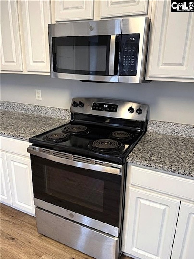 kitchen with light wood finished floors, stone counters, white cabinetry, and stainless steel appliances