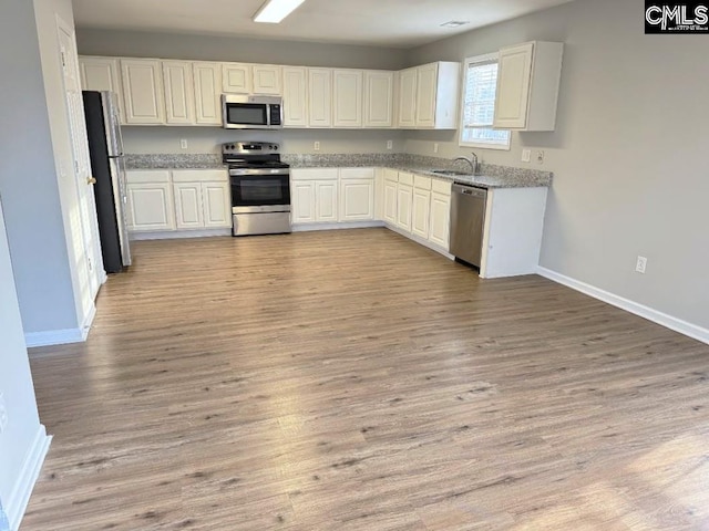 kitchen with a sink, stainless steel appliances, baseboards, and light wood finished floors