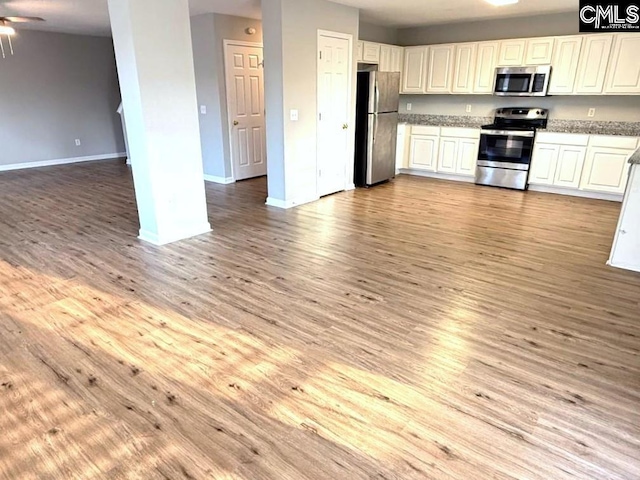 kitchen featuring baseboards, appliances with stainless steel finishes, open floor plan, and light wood finished floors