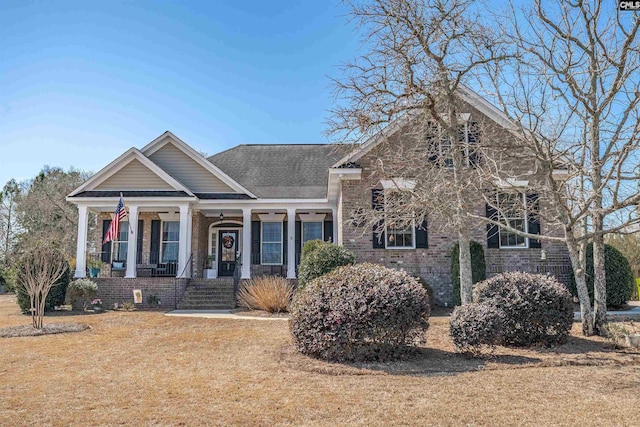 view of front of property featuring brick siding, covered porch, a front yard, and a shingled roof