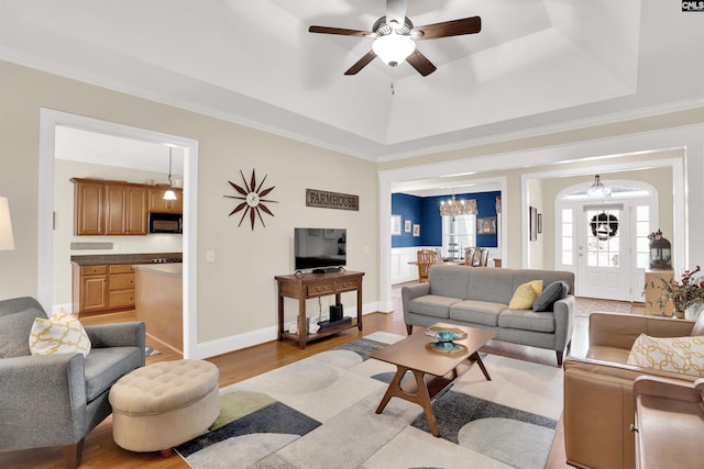 living room with a tray ceiling, baseboards, wood finished floors, and ceiling fan with notable chandelier