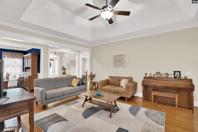 living room with ornamental molding, a raised ceiling, a ceiling fan, and wood finished floors