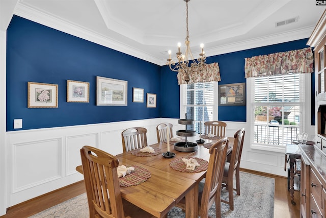 dining area featuring visible vents, a tray ceiling, wood finished floors, an inviting chandelier, and wainscoting