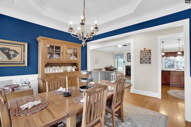 dining space featuring light wood finished floors, crown molding, a fireplace, an inviting chandelier, and a raised ceiling