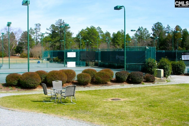 view of tennis court with a lawn and fence