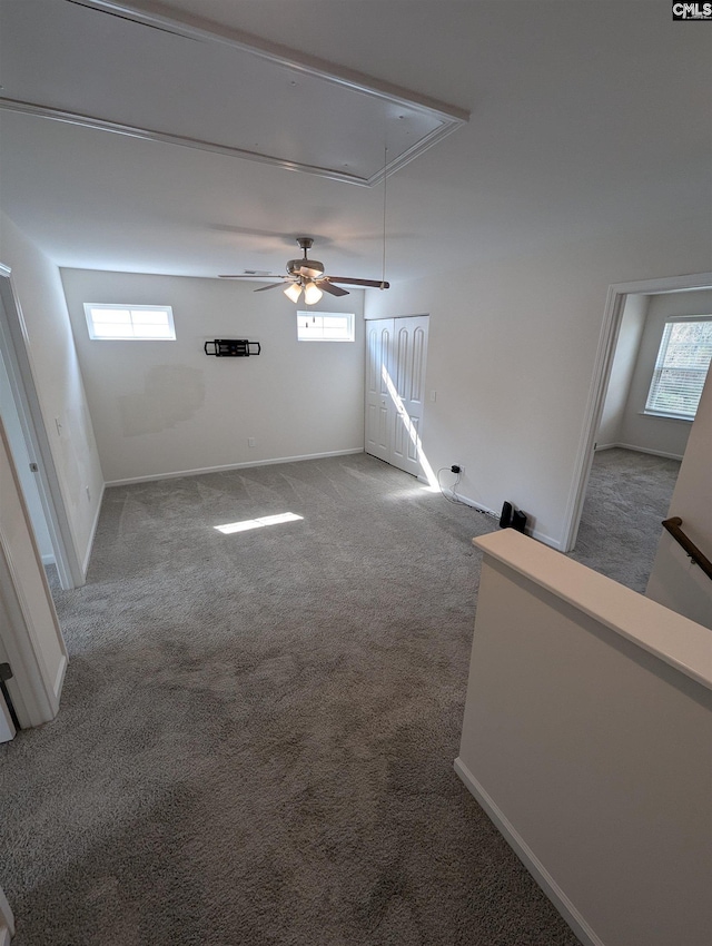 unfurnished living room featuring attic access, carpet flooring, a ceiling fan, and baseboards