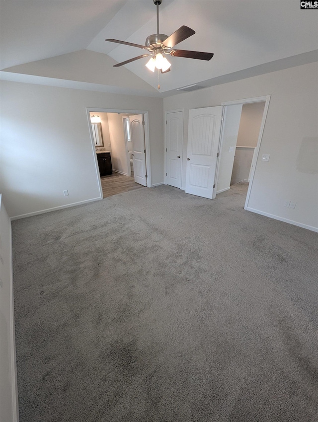 unfurnished bedroom featuring baseboards, light colored carpet, lofted ceiling, ensuite bathroom, and a ceiling fan