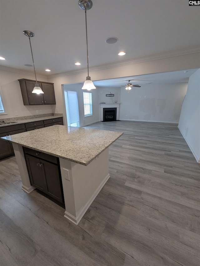 kitchen with wood finished floors, a fireplace, pendant lighting, crown molding, and a center island