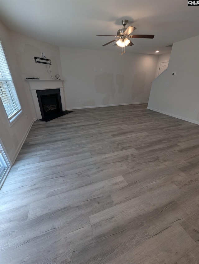 unfurnished living room featuring wood finished floors, a fireplace with flush hearth, a ceiling fan, and baseboards