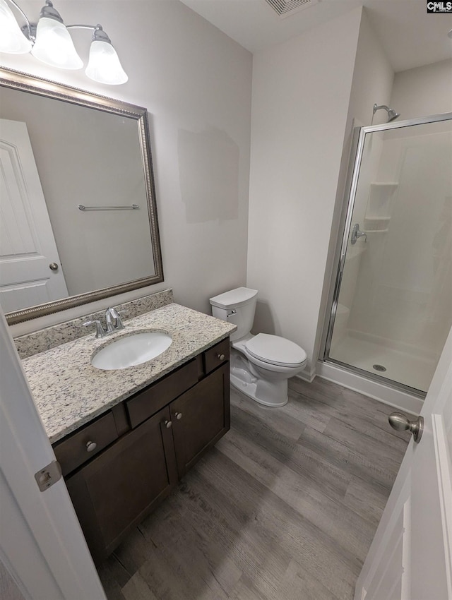 bathroom with wood finished floors, toilet, a stall shower, and vanity