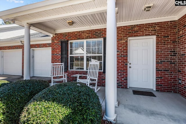 doorway to property with a porch, an attached garage, and brick siding