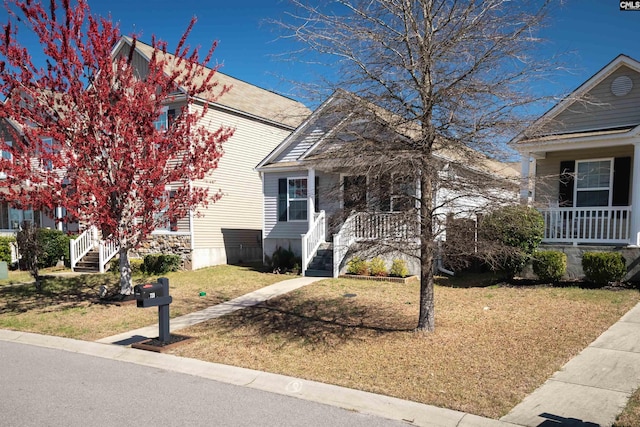 view of property hidden behind natural elements featuring a porch and a front lawn